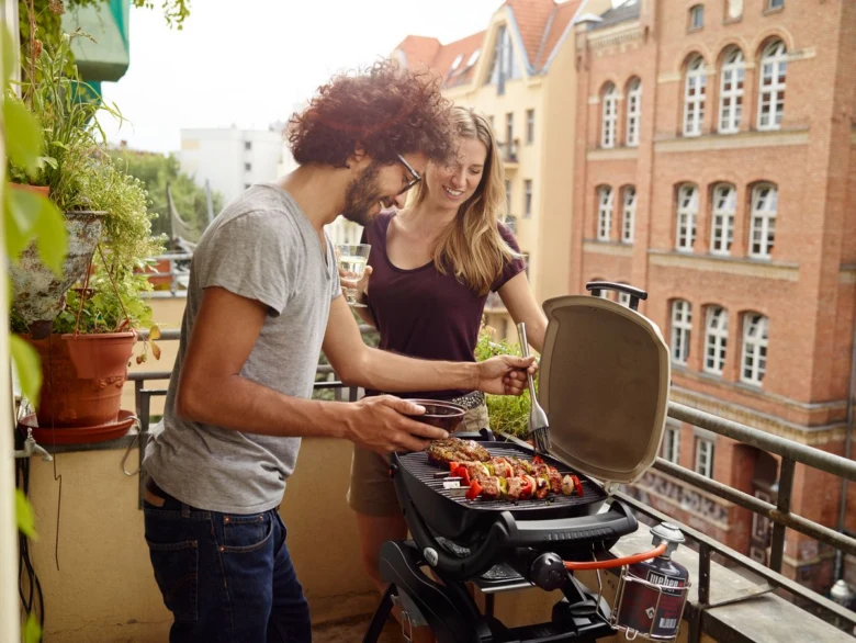 Muž a žena připravují jídlo na plynovém grilu na balkóně.
