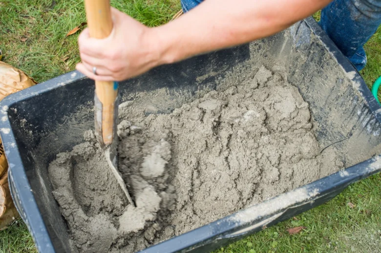Míchání betonu lopatou v vozíku na trávníku.