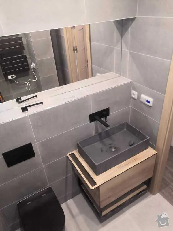 Moderní koupelna po rekonstrukci s šedými dlaždicemi a dřevěným umyvadlem.