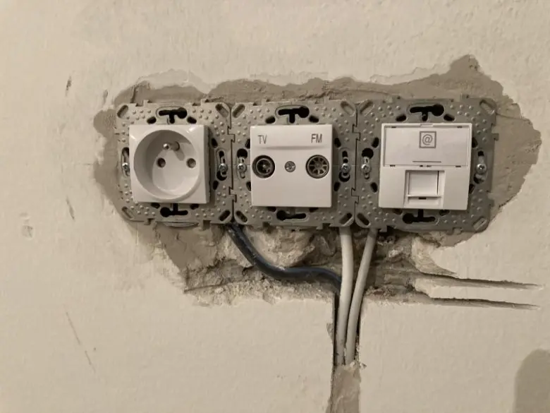 Bílá elektrická zásuvka s kabely v zdi během rekonstrukce bytu.