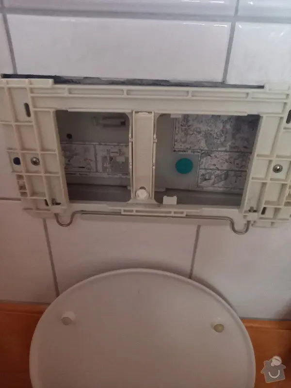 Rozložená plastová konstrukce sedátka záchodu na dlažbě pro opravu.