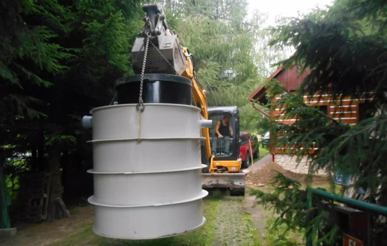 Bílá septická nádrž je zvedána křeslem během instalace venku.