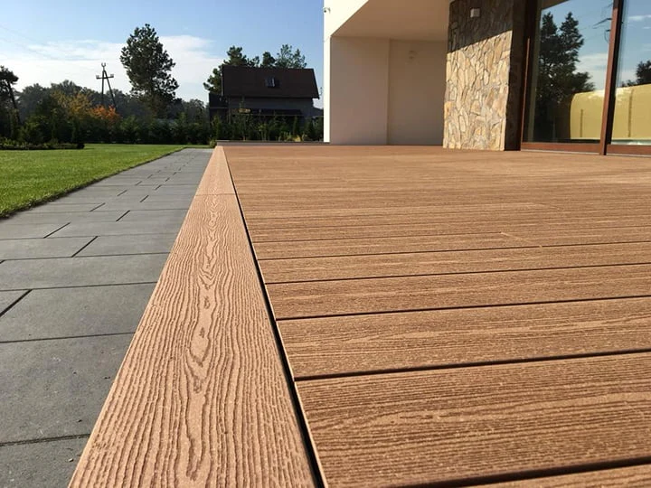 Moderní dřevěná podlaha na terase z kompozitových prken vedle dlažby.