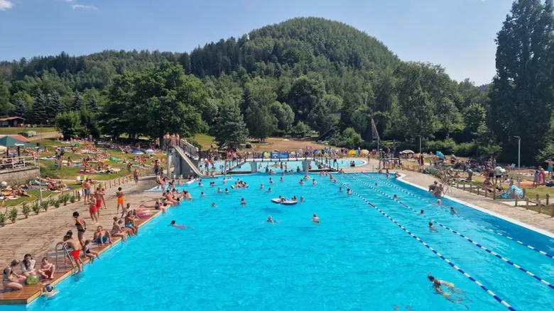 Venkovní bazén v Košťálově s plavci a okolními kopci.