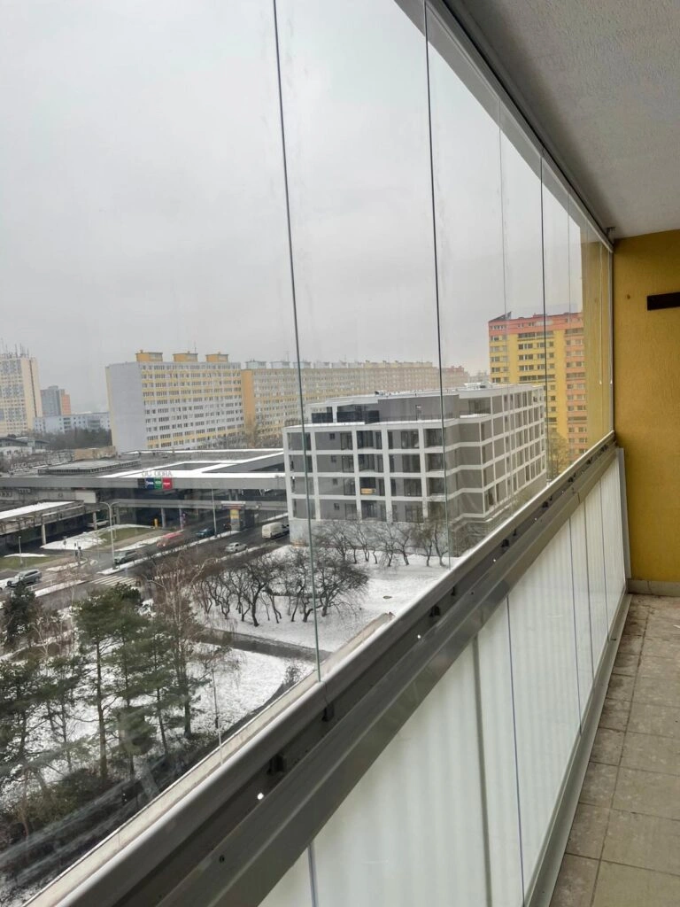 Zasklený balkon s výhledem na zasněženou ulici v Praze.