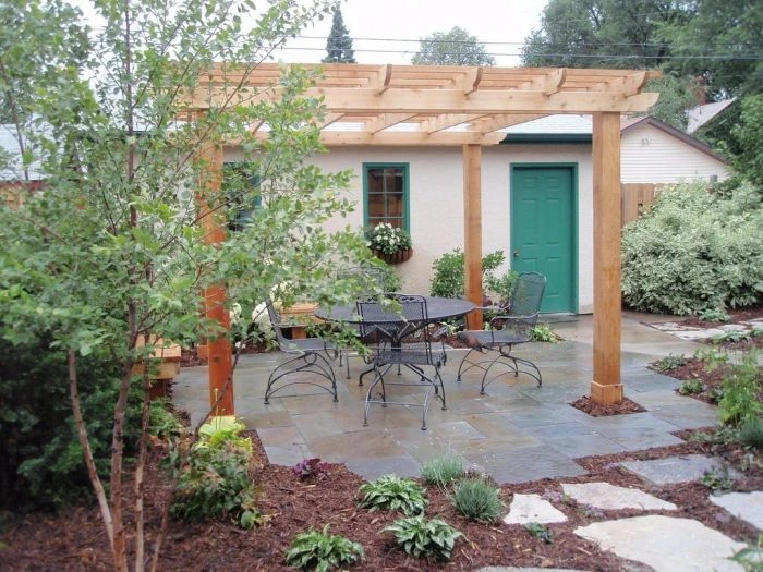 Hotová dřevěná pergola nad zahradním posezením s kamennou dlažbou.
