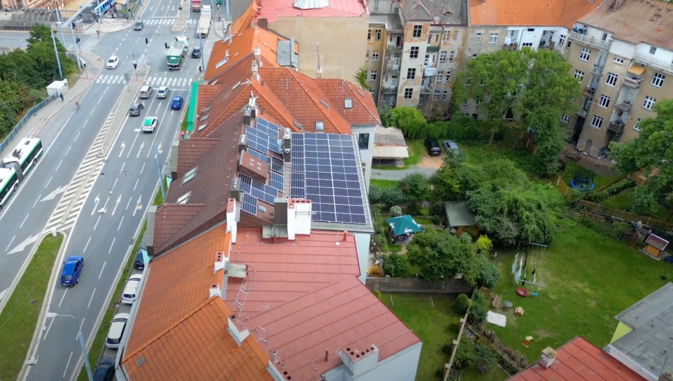 Fotovoltaické panely na střeše bytového domu v městské zástavbě.