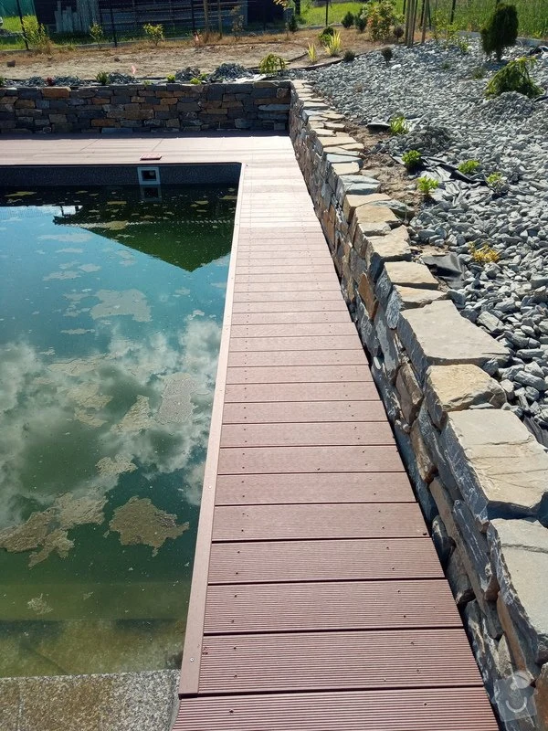 Dřevěná terasa vedle kamenného bazénu v zahradním designu.