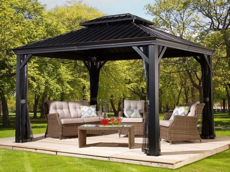 Černá zahradní pergola s nábytkem na trávníku mezi stromy.