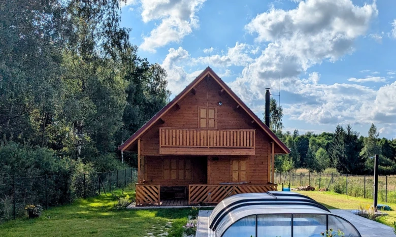 Dřevěná chata s terasou a skleníkem pro celoroční bydlení.