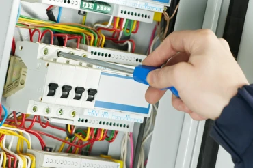 Elektrikář upravuje rozvaděč šroubovákem v elektrické skříni.