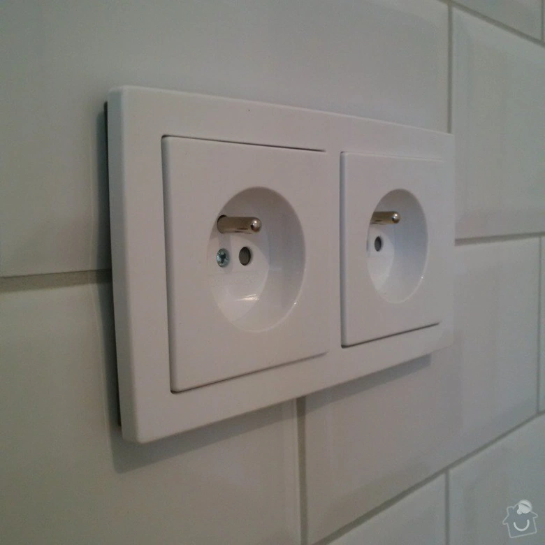 Bílá elektrická zásuvka na dlažbě v interiéru.