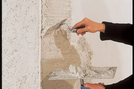 Ruční aplikace omítky na stěnu pomocí špachtle.