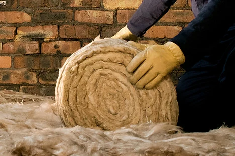 Rukou se manipuluje s válcem minerální vlny pro zateplení.