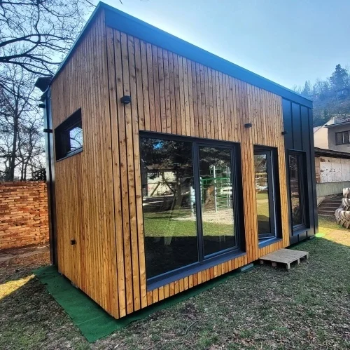Moderní dřevostavba malého domu s velkými okny venku.