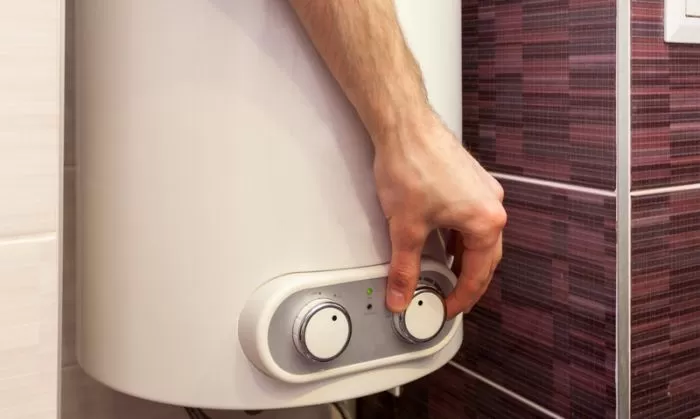 Ruka nastavuje teplotu na elektrickém bojleru v koupelně.