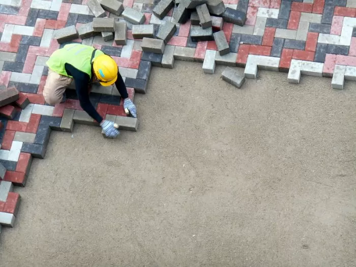 Stavebník položí dlažební kostky na betonovou terasu.