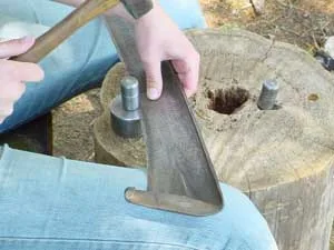 Muž kuje nůži kosy na kovové podložce.