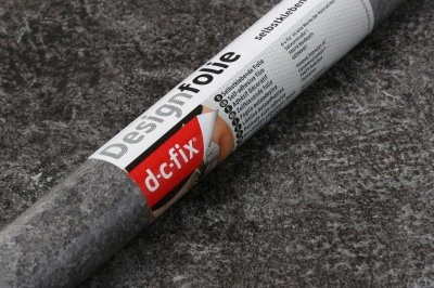Role samolepící tapety DesignFolie od značky dc-fix na šedém povrchu.