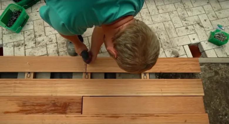 Muž montuje dřevěné prkna na terasu pomocí šroubováku.