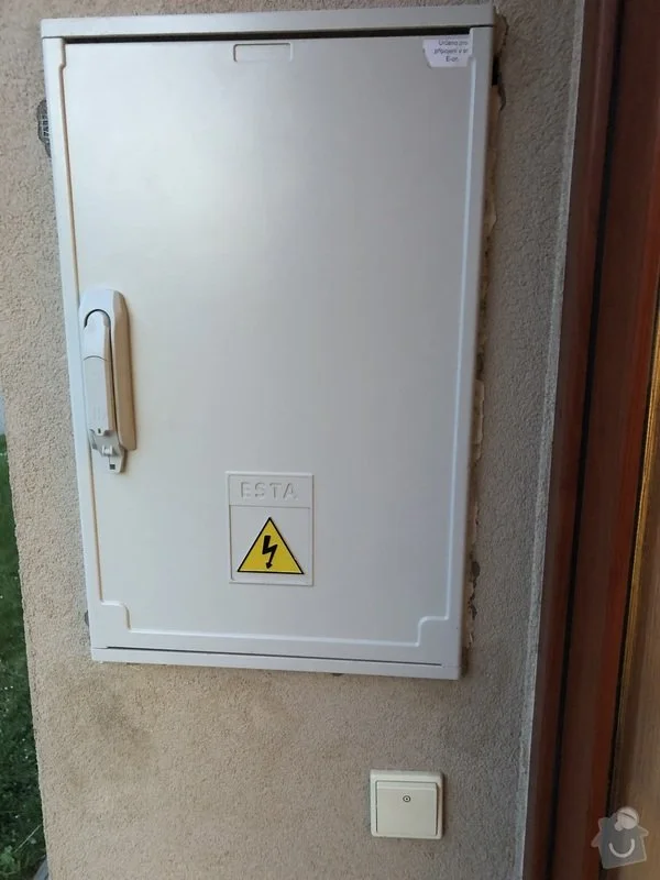 Bílá venkovní elektrická skříň s varovným štítkem na zdi.