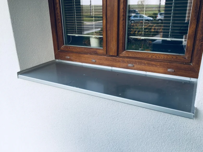 Nově nainstalovaný venkovní parapet z kovu pod dřevěným oknem.