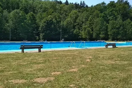 Venkovní bazén s lavičkami a lesním pozadím v létě.