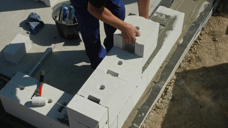 Stavebník kladí betonové bloky do zdi.