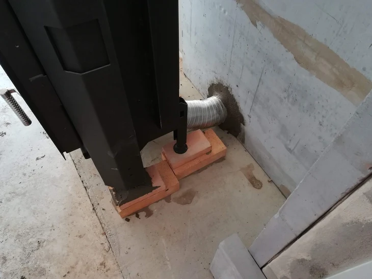 Flexibilní vzduchová hadice připojená ke krbu skrz zeď.