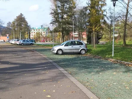 Stříbrný vůz stojí na zatravňovacích dlaždicích v parkovišti.